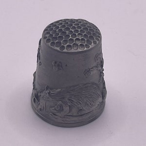 May include: A silver thimble with a honeycomb pattern on the top and a squirrel design on the side.