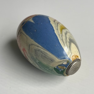 May include: An egg-shaped thimble with a marbled design in blue, white, green, and gray. The thimble has a silver metal cap on one end. The thimble is approximately 1.5 inches long.