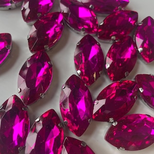 May include: Marquise-shaped hot pink rhinestones with silver-colored metal settings. The faceted gems reflect light, creating a sparkling effect. These decorative embellishments are ideal for crafting and jewelry making.