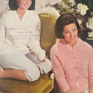 May include: Two women wearing crocheted cardigans, one in white and one in pink, are sitting on a chair. The woman in the white cardigan is holding a glass of milk. The text "Wool Shop 26, Bournville Lane Birmingham 30" is visible on the white cardigan. The text "Model A" is visible on the chair.