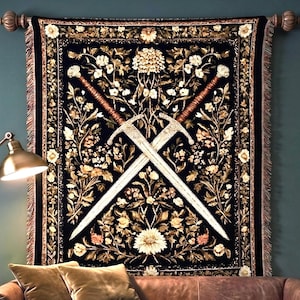 May include: A rectangular woven wall tapestry featuring a black background with a central design of two crossed silver swords surrounded by intricate floral patterns in shades of gold, cream, and muted orange, finished with a decorative fringe border.
