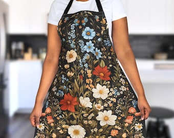 May include: A black apron with a floral print featuring red, white, blue, and green flowers. The apron has adjustable straps and a large pocket.