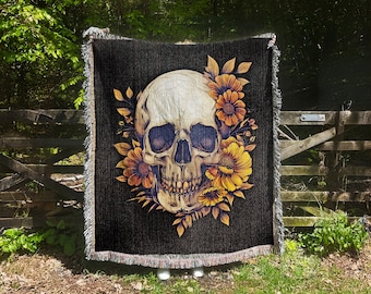 May include: A black woven throw blanket with a white skull design surrounded by yellow sunflowers.