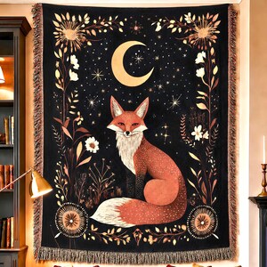 May include: A rectangular woven wall tapestry featuring a central illustration of a red fox sitting against a black background. The design includes a large yellow crescent moon, scattered stars, and floral motifs along the sides with fringed edges.