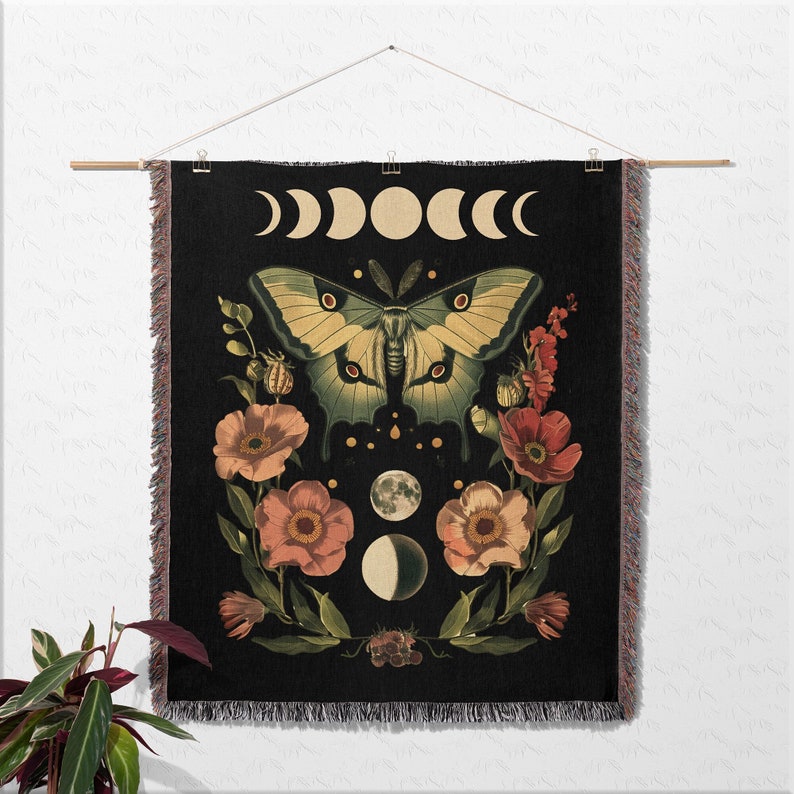 May include: A black tapestry featuring a green and yellow butterfly, pink flowers, and a crescent moon design. The tapestry is woven with a fringed border.