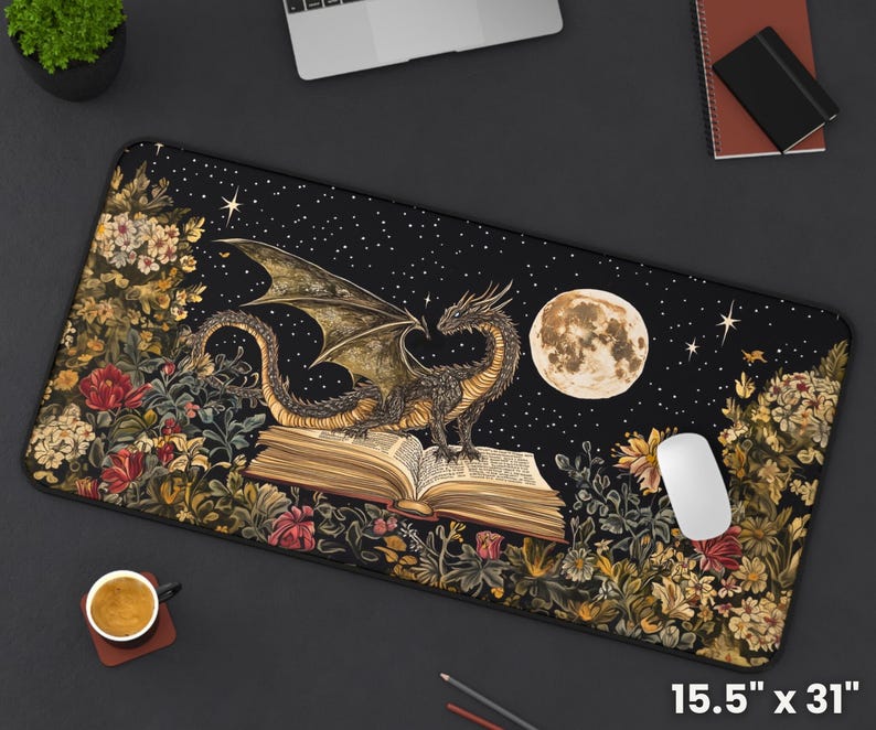 May include: A black mouse mat with a dark background featuring a dragon curled around an open book. The dragon is a dark green and gold colour with a light green underbelly. The book is open to a page with text and has a brown leather cover. The background is a dark blue with stars and a full moon. The mouse mat is 15.5 inches by 31 inches.