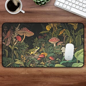 May include: Rectangular mousepad featuring a detailed illustration of a forest scene with mushrooms, a frog, and various plants. The color palette includes greens, reds, and browns, creating a whimsical and natural aesthetic. A white mouse rests on the pad.