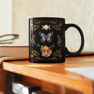 Black ceramic coffee Mug with cottagecore moon phases and moth with mushrooms.