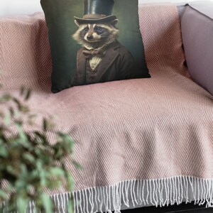 May include: A throw pillow with a vintage-style illustration of a raccoon wearing a top hat and bow tie. The background is a dark green color.