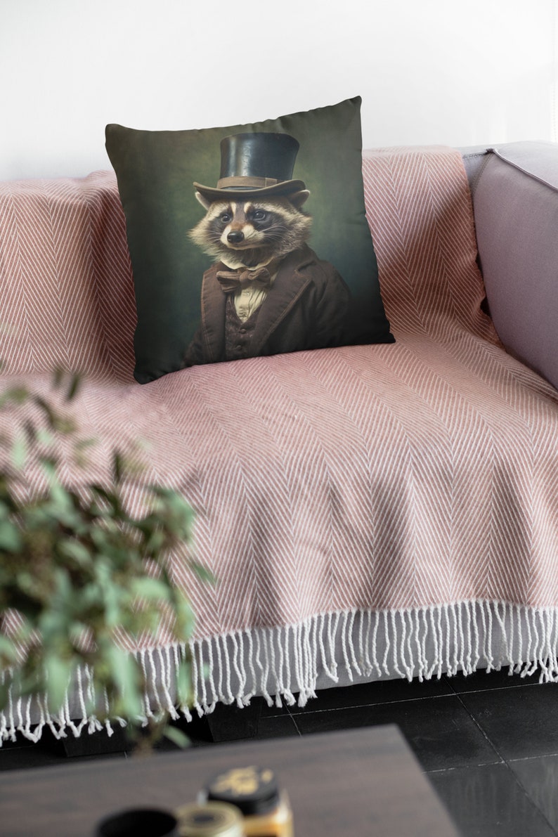 May include: A throw pillow with a vintage-style illustration of a raccoon wearing a top hat and bow tie. The background is a dark green color.