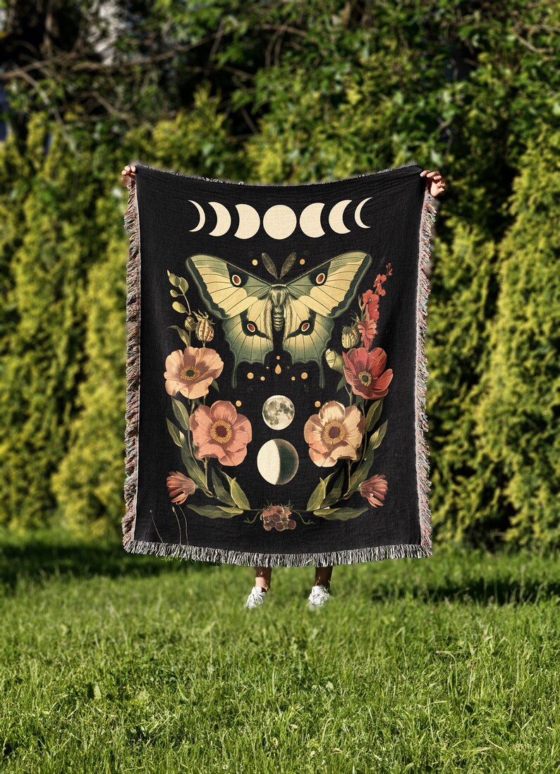 Woven tapestry blanket with a green luna moth, moon phases, and floral accents.