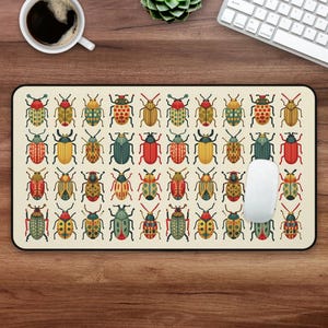 Pode incluir: Um tapete de rato bege com um padrão colorido de 36 besouros. Os besouros estão em filas de seis e são todos de cores e designs diferentes. O tapete de rato é retangular e tem uma borda preta.