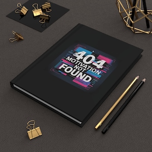 May include: Black journal featuring the text "404 Motivation Not Found" in a glitch design. Gold and black stationery, including paper clips and pencils, are arranged around the journal.