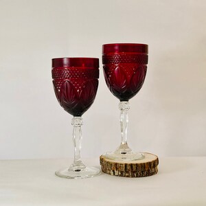May include: Two red wine glasses with a cut glass design. The glasses are on a wooden coaster.