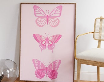Pode incluir: Uma impressão emoldurada com três borboletas cor-de-rosa sobre um fundo rosa claro. As borboletas estão dispostas verticalmente, com a maior borboleta no topo e a menor na parte inferior.