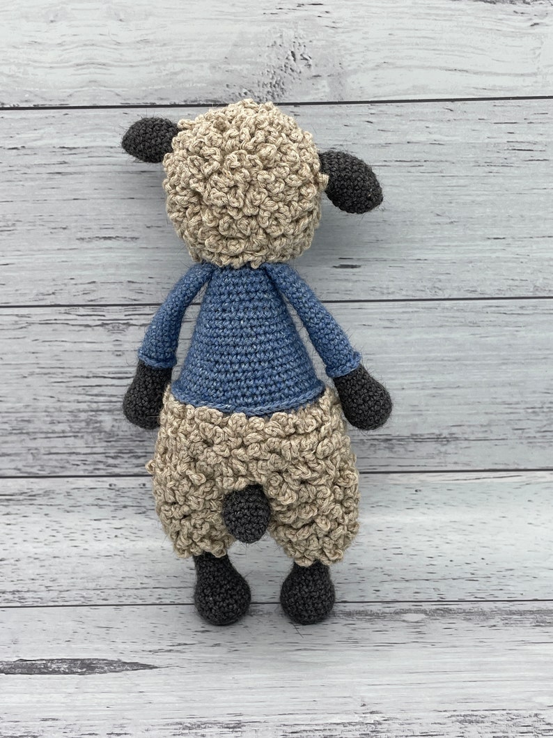 May include: A crocheted stuffed sheep toy with a blue shirt. The sheep has a brown face and black hooves.
