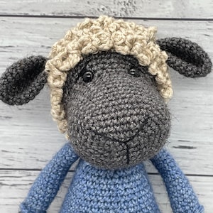 May include: A crocheted sheep toy with a gray body, black ears, and a cream-colored fleece. The sheep is wearing a blue knitted sweater.