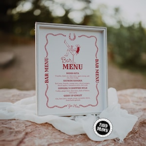 Puede incluir: Un menú de bar enmarcado con temática de rodeo. El menú presenta un diseño rojo y blanco con una herradura y una ilustración de vaquera. El menú enumera opciones de bebidas como "Rodeo Rita" y "Cowgirl's Campfire Mule". Es visible una pegatina "Hand Drawn".