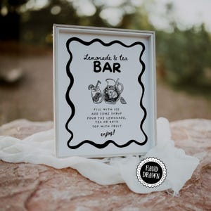 Può includere: Un cartello incorniciato con un design in bianco e nero che recita "Lemonade & tea BAR". Il cartello include illustrazioni di una brocca e un bicchiere di limonata. Il testo sottostante spiega come preparare le bevande. Un adesivo "Hand Drawn" si trova in basso a destra.