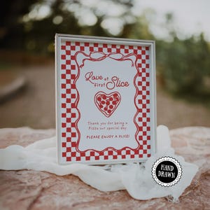 May include: A framed sign with a red and white checkered border and the words "Love at first Slice." The sign features a heart-shaped pizza illustration and the text "Thank you for being a Pizza our special day. Please enjoy a slice!"