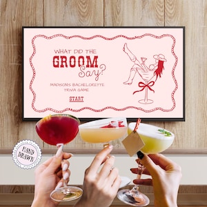 May include: A framed pink bachelorette party game board with the text "What Did The Groom Say?" and a cartoon illustration. Three cocktails in stemmed glasses are held up in a toast.