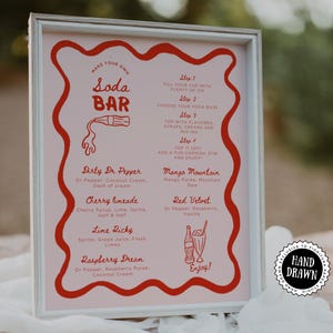 May include: A framed pink sign with red text and illustrations, advertising a soda bar. The sign includes instructions and drink recipes like "Dirty Dr. Pepper" and "Cherry Limeade." A "Hand Drawn" sticker is in the corner.