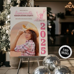 May include: A graduation party sign on an easel features a photo of a person wearing a cowboy hat. The sign reads "Welcome to Savannah's Graduation Party, Class of 2025." Silver disco balls are in the foreground.