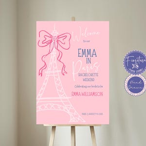 Puede incluir: Un cartel de bienvenida rosa con una Torre Eiffel blanca y un lazo rosa. El texto dice "Bienvenido a nuestro Emma en París Fin de semana de despedida de soltera Celebrando a nuestra novia Emma Williamson París 13 de agosto de 2023".