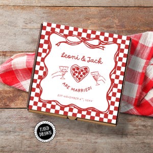 May include: A pizza box with a red and white checkered pattern and a red decorative border. The box features the text "Leoni & Jack ARE MARRIED!" with a heart-shaped pizza illustration. The box is on a wooden surface with a red and white checkered cloth.