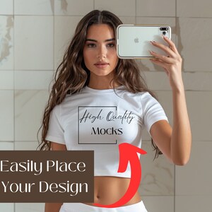 May include: A white crop top with short sleeves and the text "High Quality Mocks" printed on the front. The model is holding a white smartphone with a gold frame.