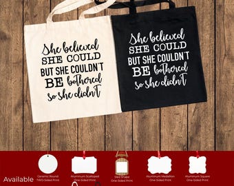 May include: Two canvas tote bags, one cream and one black, with the quote "She believed she could but she couldn't be bothered so she didn't" printed in white. The image also shows various other products with the same design.
