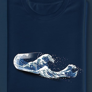 Puede incluir: Camiseta azul marino con un diseño gráfico de olas saliendo de un vaso. El diseño de las olas es en tonos azules y blancos, creando un efecto visual dinámico en la camiseta doblada.