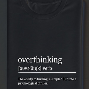 Peut inclure: T-shirt noir avec le mot "overthinking" en blanc, sa prononciation phonétique et sa définition. La définition est : "La capacité de transformer un simple "OK" en thriller psychologique."