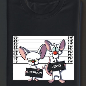 May include: Black t-shirt with a cartoon graphic of two mice in a police lineup. One mouse holds a sign saying "THE BRAIN", the other holds a sign saying "PINKY". The background includes height measurements in feet and inches.
