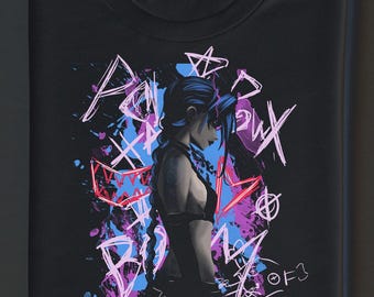 May include: Black t-shirt with a graphic design of a character with blue hair and a tattoo. The design includes graffiti-style text and colourful paint splatters in pink, blue, and white. The t-shirt is folded.