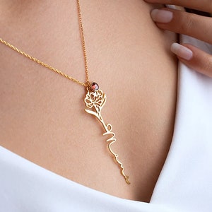 May include: Gold necklace with a delicate flower pendant and a red gemstone. The pendant is shaped like a flower with a stem that forms the word "Mom".