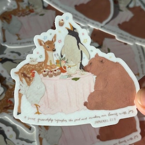 May include: A sticker featuring a whimsical tea party scene with a deer, penguin, bear, and chicken around a pink table. The sticker has a white border and includes the text "A sweet friendship refreshes the soul and awakens our hearts with joy PROVERBS 27:9."