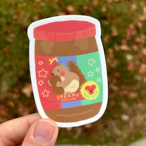 May include: A sticker of a peanut butter jar with a cartoon squirrel holding a peanut. The jar is labelled "Creamy Peanut Butter" and "Made with ♥". The jar is decorated with red, blue and green stars.