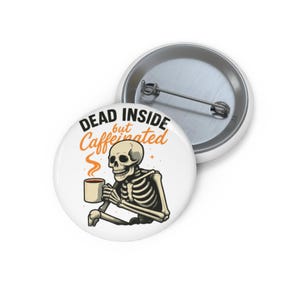 May include: White button featuring a skeleton holding a coffee mug. The text reads "DEAD INSIDE but Caffeinated" in black and orange. The skeleton is beige and the coffee mug is tan.