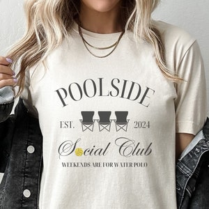 Pode incluir: Uma camiseta bege com o texto "Poolside Social Club Est. 2024" e um gr&aacute;fico de tr&ecirc;s cadeiras de praia com uma bola de voleibol. O texto "Weekends are for water polo" est&aacute; abaixo do gr&aacute;fico.