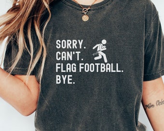 May include: A dark gray t-shirt with the text "SORRY. CAN'T. FLAG FOOTBALL. BYE." in white lettering. A stick figure running with a flag is also printed on the shirt.