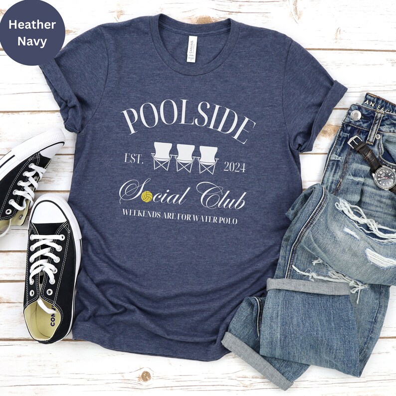Pode incluir: Uma camiseta azul marinho heather com um design gr&aacute;fico branco que diz "Poolside Social Club Est. 2024" com uma ilustra&ccedil;&atilde;o branca de tr&ecirc;s cadeiras de praia e uma bola de v&ocirc;lei amarela. O texto abaixo do gr&aacute;fico diz "Weekends are for water polo."