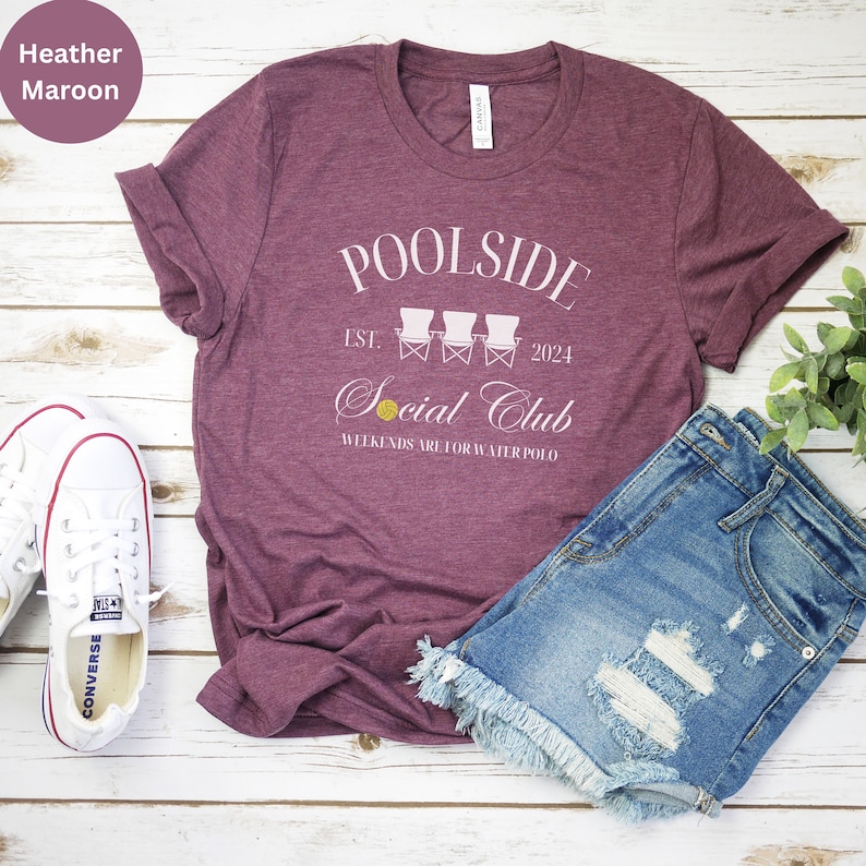 Pode incluir: Camiseta heather marrom com texto branco que diz "Poolside Est. 2024 Social Club Weekends are for Water Polo". O texto &eacute; cercado por tr&ecirc;s cadeiras de praia brancas.