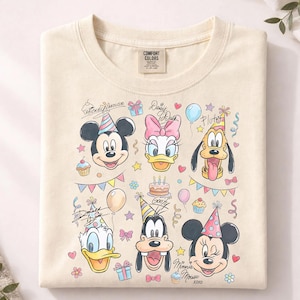 May include: Cream-colored sweatshirt featuring cartoon characters Mickey Mouse, Minnie Mouse, Donald Duck, Daisy Duck, Pluto, and Goofy. The design includes birthday party elements like balloons, cupcakes, and confetti. The brand tag "Comfort Colors" is visible.