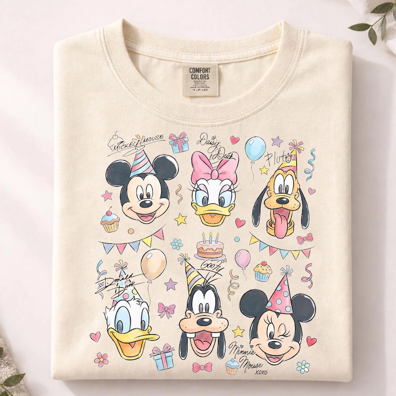 May include: Cream-colored sweatshirt featuring cartoon characters Mickey Mouse, Minnie Mouse, Donald Duck, Daisy Duck, Pluto, and Goofy. The design includes birthday party elements like balloons, cupcakes, and confetti. The brand tag "Comfort Colors" is visible.