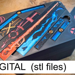 May include: A black, rectangular box with colorful, stylized designs and the text "DIGITAL (stl files)". The box has several slots with blue, red, and orange accents. A separate card with a red emblem is visible.