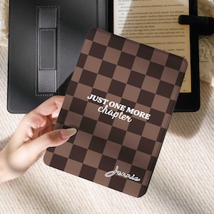 Può includere: Una custodia per e-reader a scacchi marrone e bianca con la scritta "JUST ONE MORE chapter" e il nome "Jennie" in corsivo. La custodia è tenuta davanti a un e-reader nero e a una custodia nera.