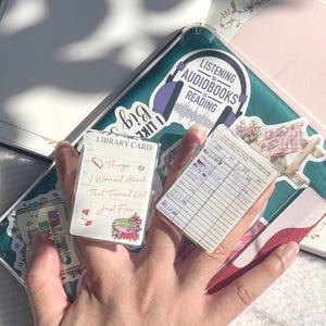 May include: Two clear acrylic rings, one with a library card design and the text "LIBRARY CARD", "Things I Worried About That Turned Out Just Fine". The other ring has a vintage library card design. The rings are on a background with stickers and the text "LISTENING to AUDIOBOOKS is READING".