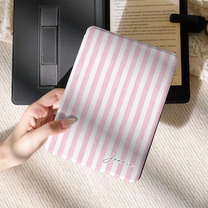 May include: An e-reader device featuring a protective cover with a light pink and white vertical striped pattern. The cover displays the name Jennie in a black cursive script. The device is open, revealing a black interior and a screen with text.