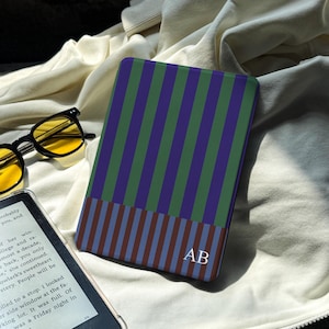 May include: A rectangular e-reader case featuring a vertical striped pattern in purple and green on the top section and a smaller horizontal striped pattern in brown and blue on the bottom, with the white monogram letters AB printed on the lower right.